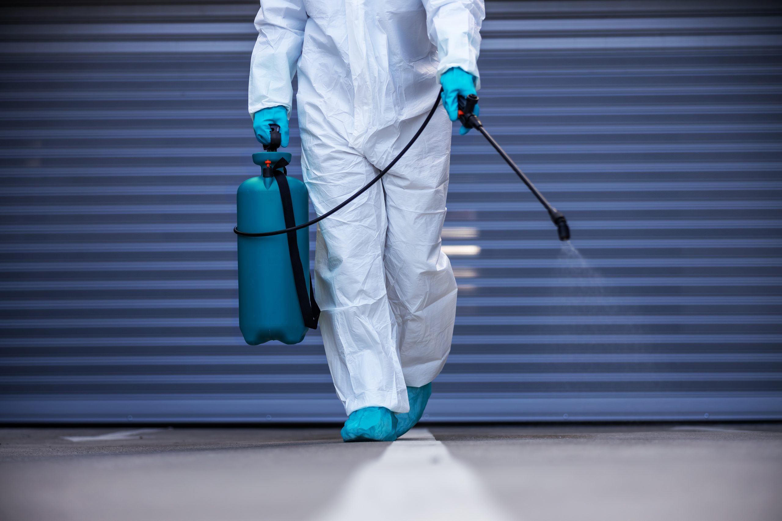 Technician in protective suit and mask performing biohazard disinfection
